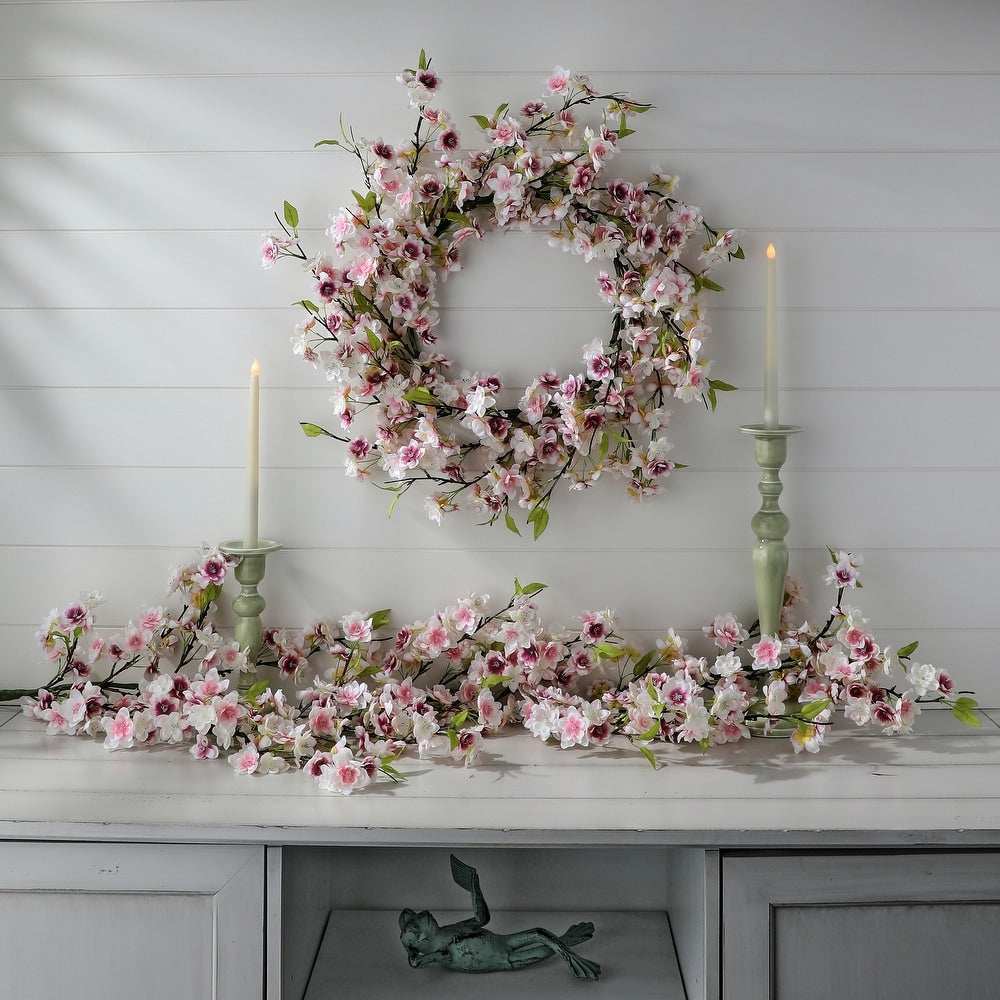 Round plastic wreath with soft pink cherry blossom flowers and green foliage on a white background.