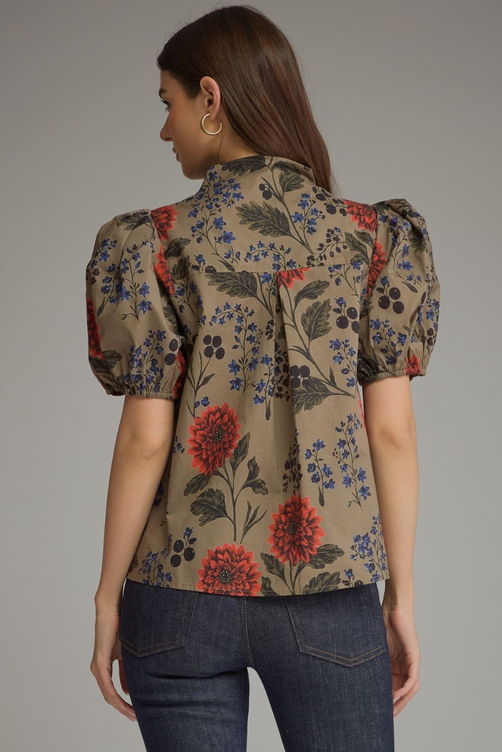 Back view of a woman wearing a khaki Amanda floral short puff sleeve top with dark blue jeans.