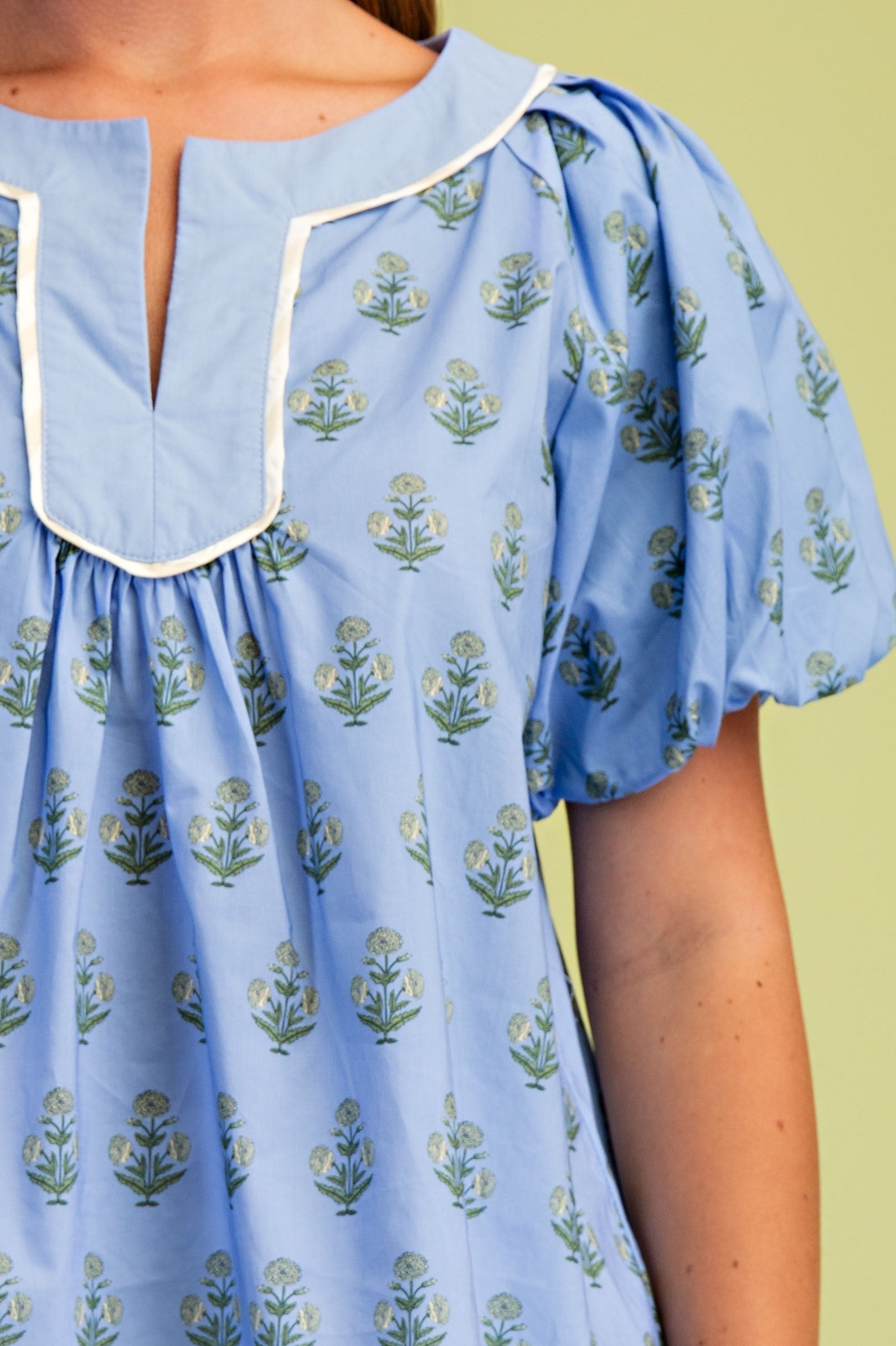 Close-up of a light blue Hannah floral printed blouse with a notch neck and short puff sleeves.