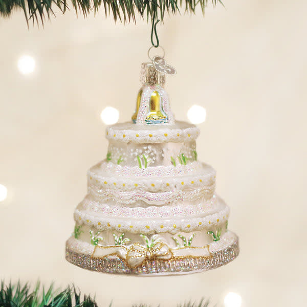 White ceramic Christmas ornament shaped like a tiered wedding cake with green holly accents.