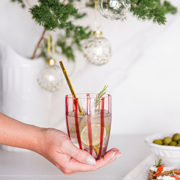 Hand holding a Nuovo Stripe Red Tall Tumbler with a lime slice, rosemary, and gold straw.