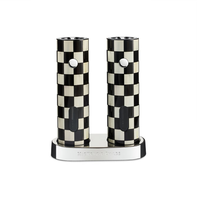 Two black and white checkered electric salt and pepper grinders on a silver charging base.