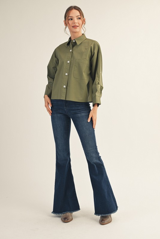 Woman wearing an olive green Clarisse button down shirt with multi-fold sleeves and flare jeans.