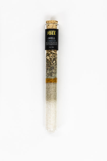 Glass vial containing mineral-rich sea salts with botanicals inside a mesh soaking pouch.