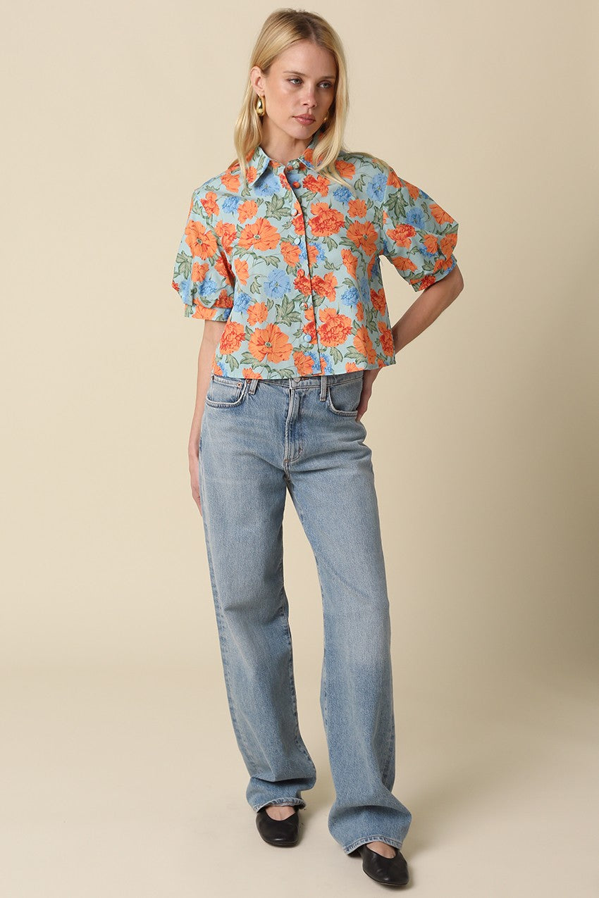 Woman wearing a Mollie blue and orange floral puff-sleeve button top with light wash jeans.