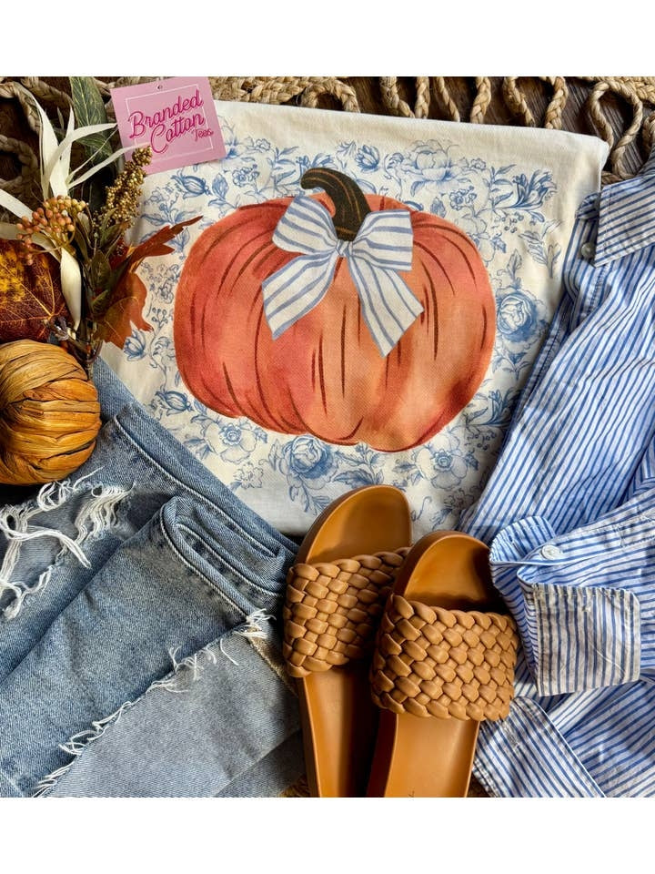 White top with a large orange pumpkin graphic, blue floral background, and a striped blue bow.