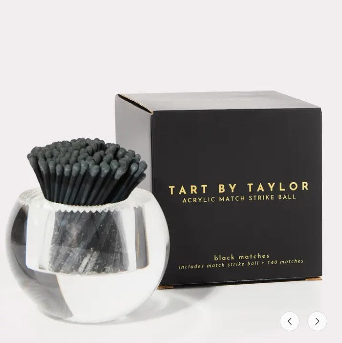 Acrylic match strike ball with black matches next to its black and gold branded box.