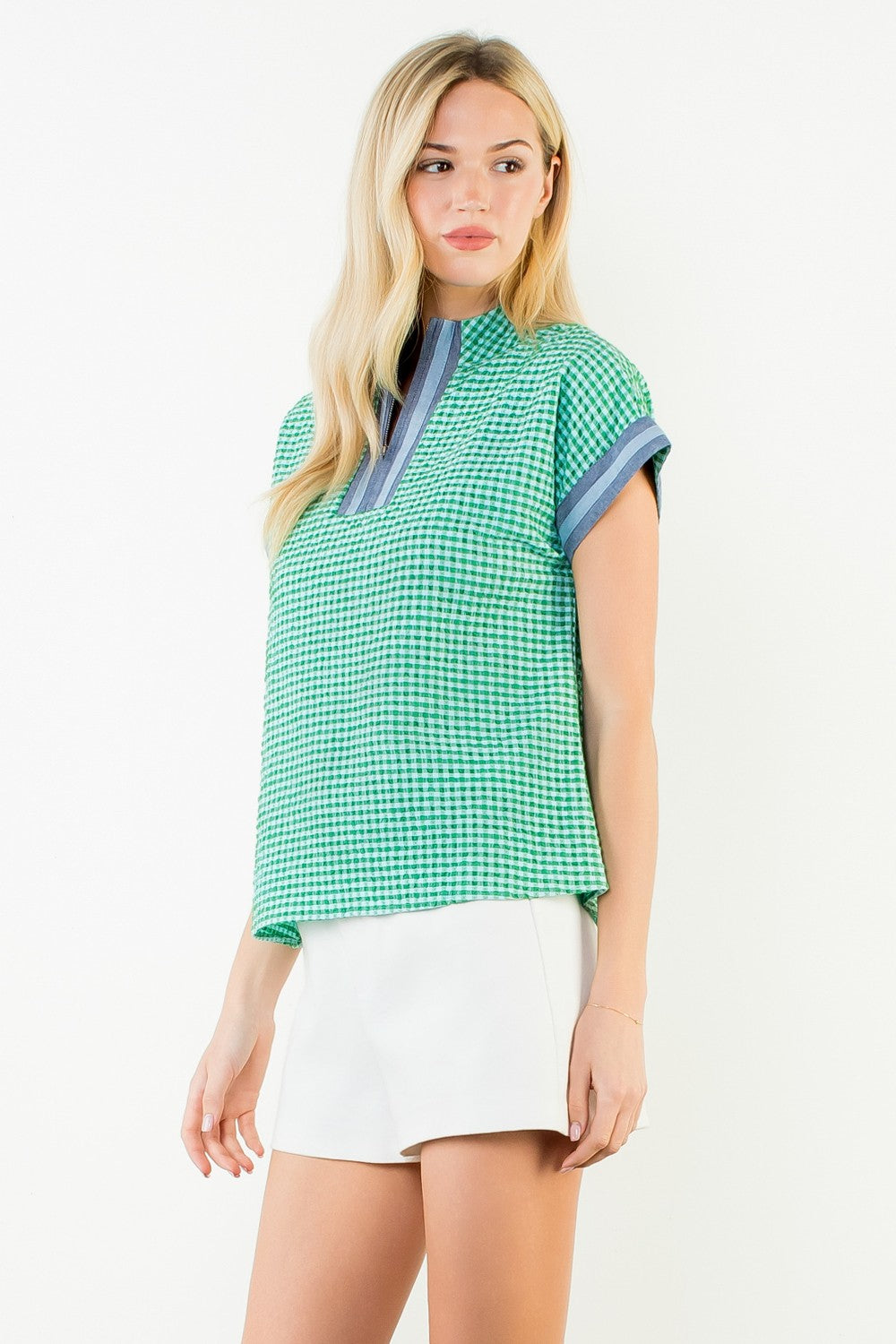 Woman wearing a green and white Ariana short sleeve gingham patterned top with white shorts.