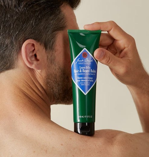 A man holds a green tube of Jack Black Leave It In Hair & Beard Balm against his shoulder.