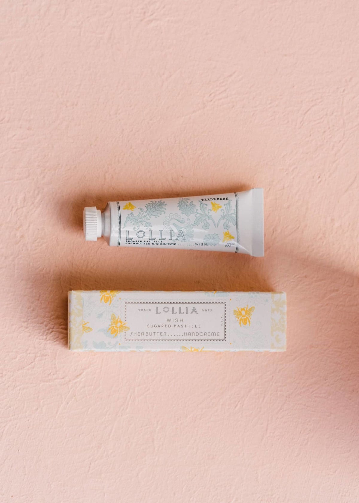 Petite Wish hand cream with golden bee illustration on blue French foulard pattern packaging.