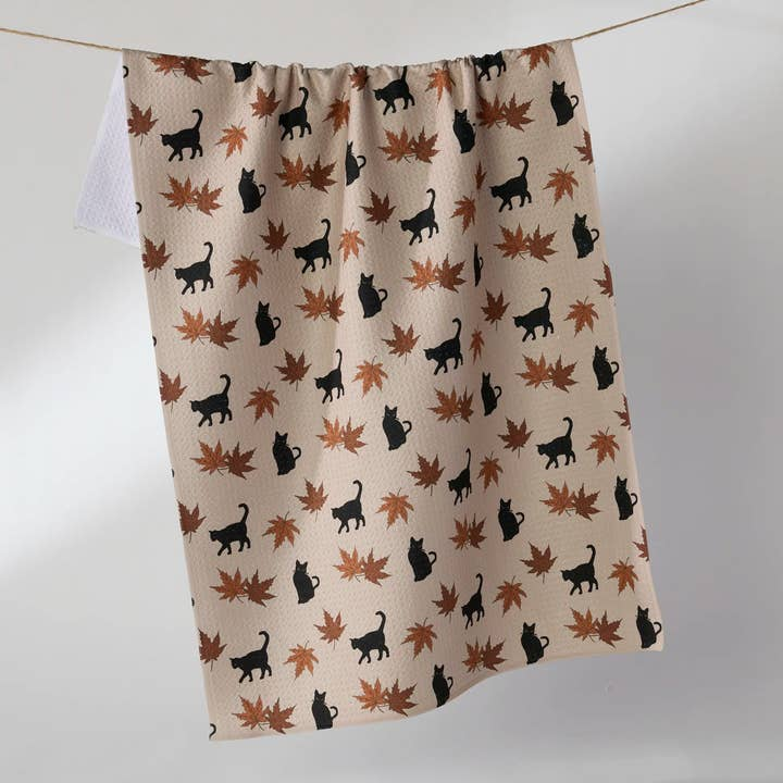Waffle weave Halloween tea towel with a pattern of black cats and orange maple leaves.