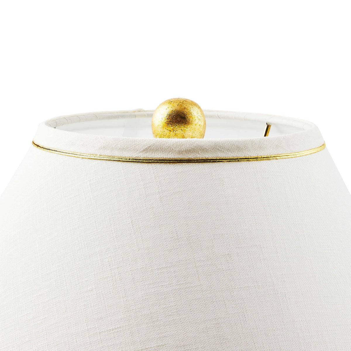 Close-up of the Flutter Table Lamp's white hardback shade with gold trim and brass leaf finial.