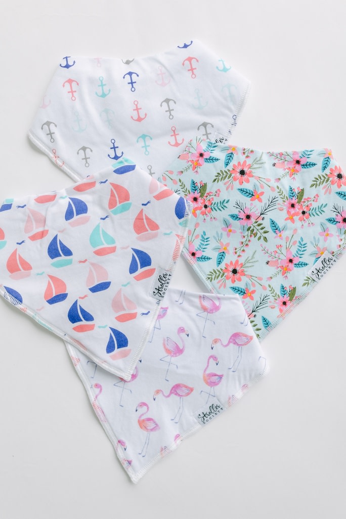 Four baby bandana bibs with anchor, sailboat, floral, and flamingo patterns on a white background.