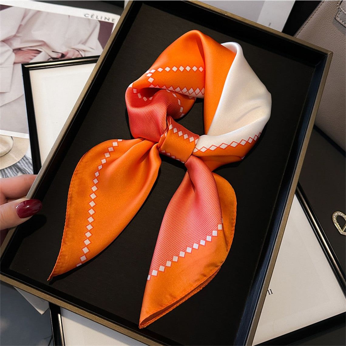 70cm orange and white geometric print silk-like scarf tied in a knot on a black tray.