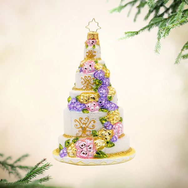White tiered cake ornament with pink, purple, and gold flowers and a gold star topper.