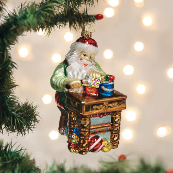 Red ceramic Santa ornament with white beard, black hat trim, holding a toy hammer in workshop setting.