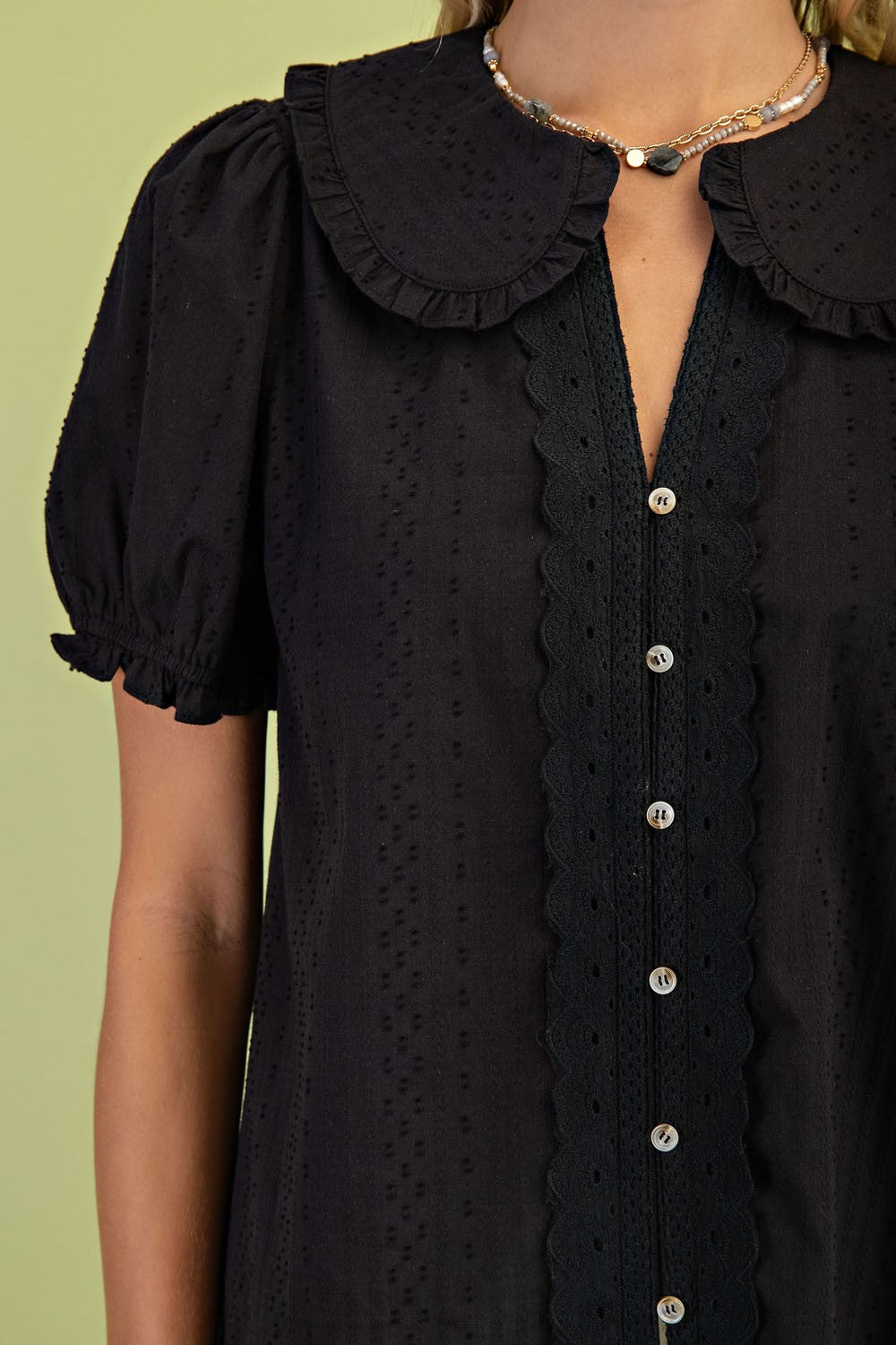 Close-up of a black cotton blouse with a Peter Pan collar, puff sleeves, and button-down front.
