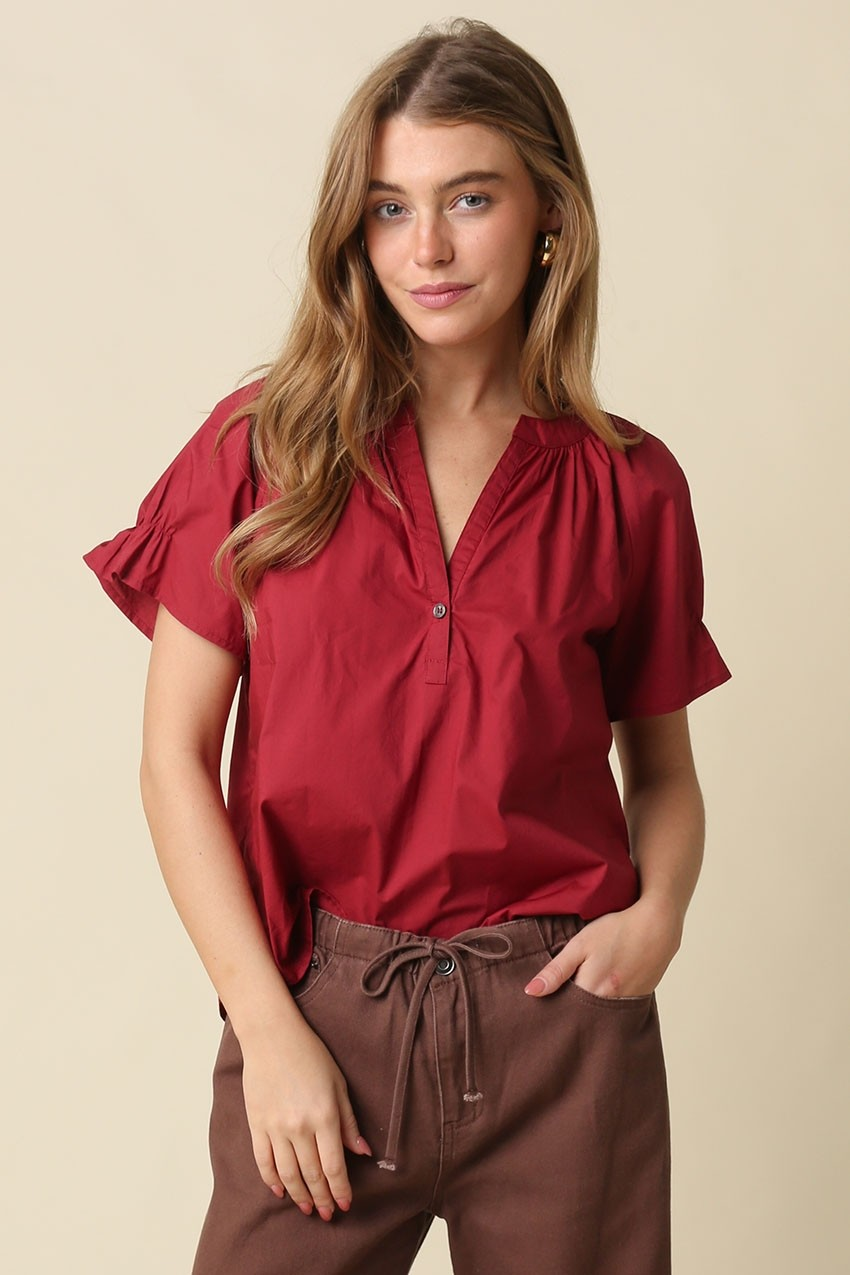 Woman wearing a red Hylee Ruffle Sleeve Peasant Blouse with a split neckline and brown pants.
