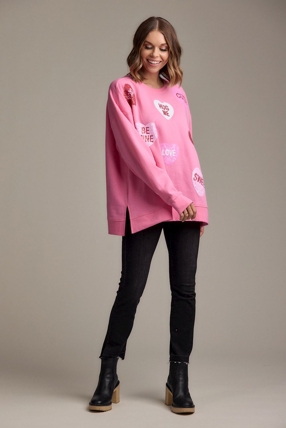 Woman wearing a Pink Valentine's Sparkle Sweatshirt with heart graphics and black pants.