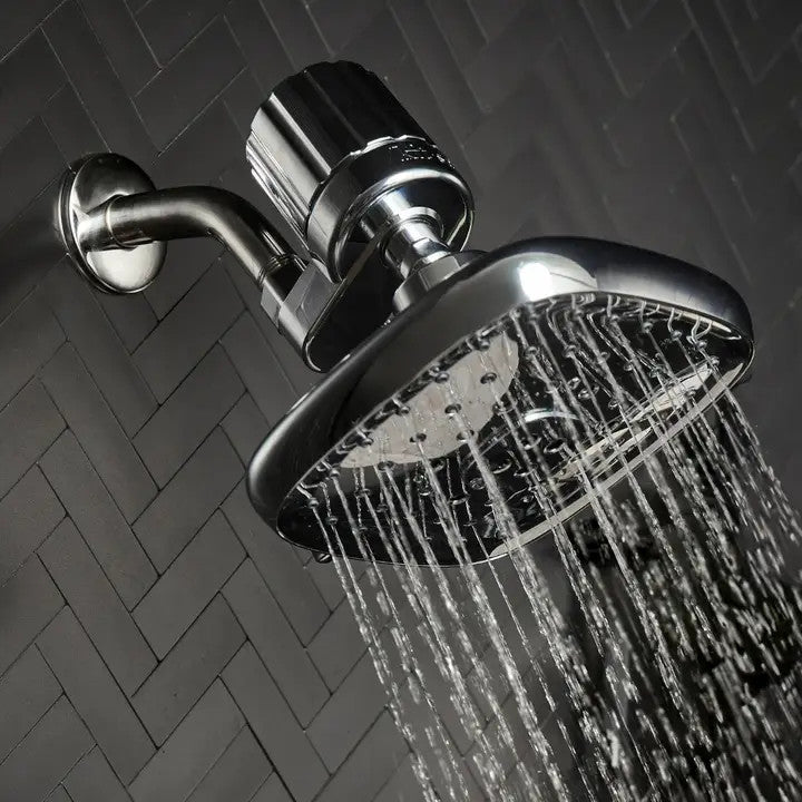 Chrome shower filter attached to a wall-mounted shower head with water flowing against dark tiles.