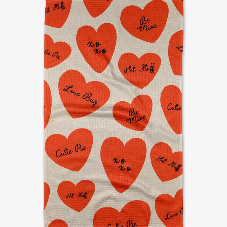 Waffle weave kitchen tea towel with red conversation hearts and romantic phrases on a white base.