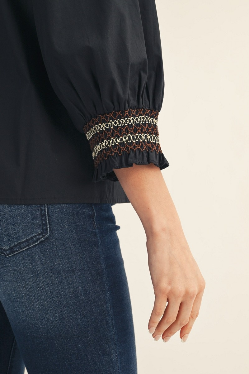 Close-up of a black top's 3/4 puff sleeve featuring brown and cream embroidered smocking cuffs.