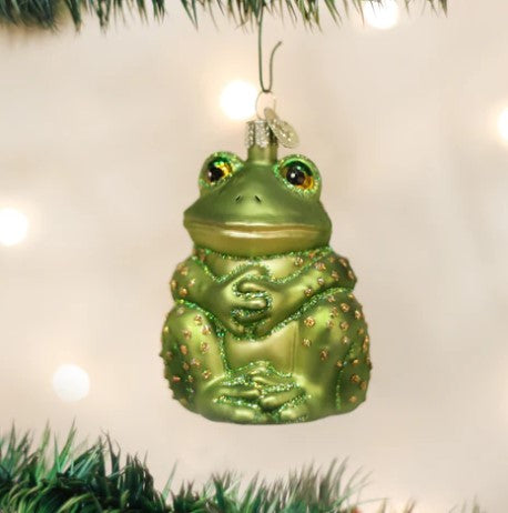 Green glass sitting frog ornament with glitter accents hanging on a Christmas tree.