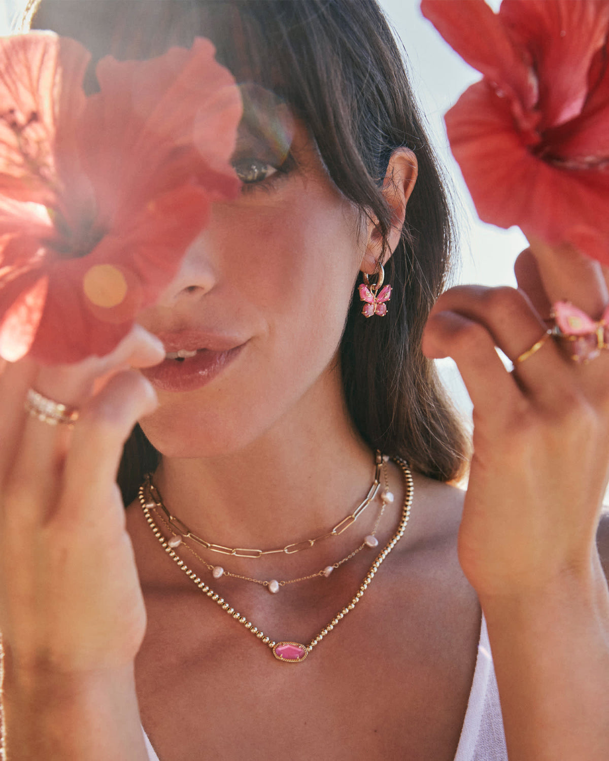 Woman wearing Bianca Butterfly Huggie Earrings with pink charms and layered gold necklaces.