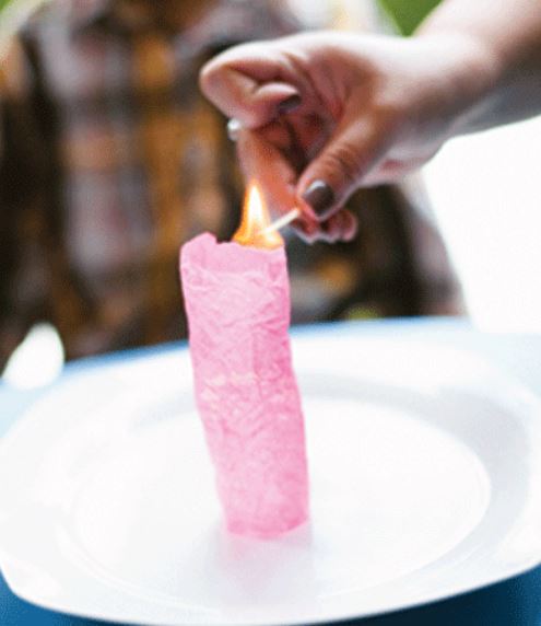 Pink wish paper candle being lit with a match on a white plate.