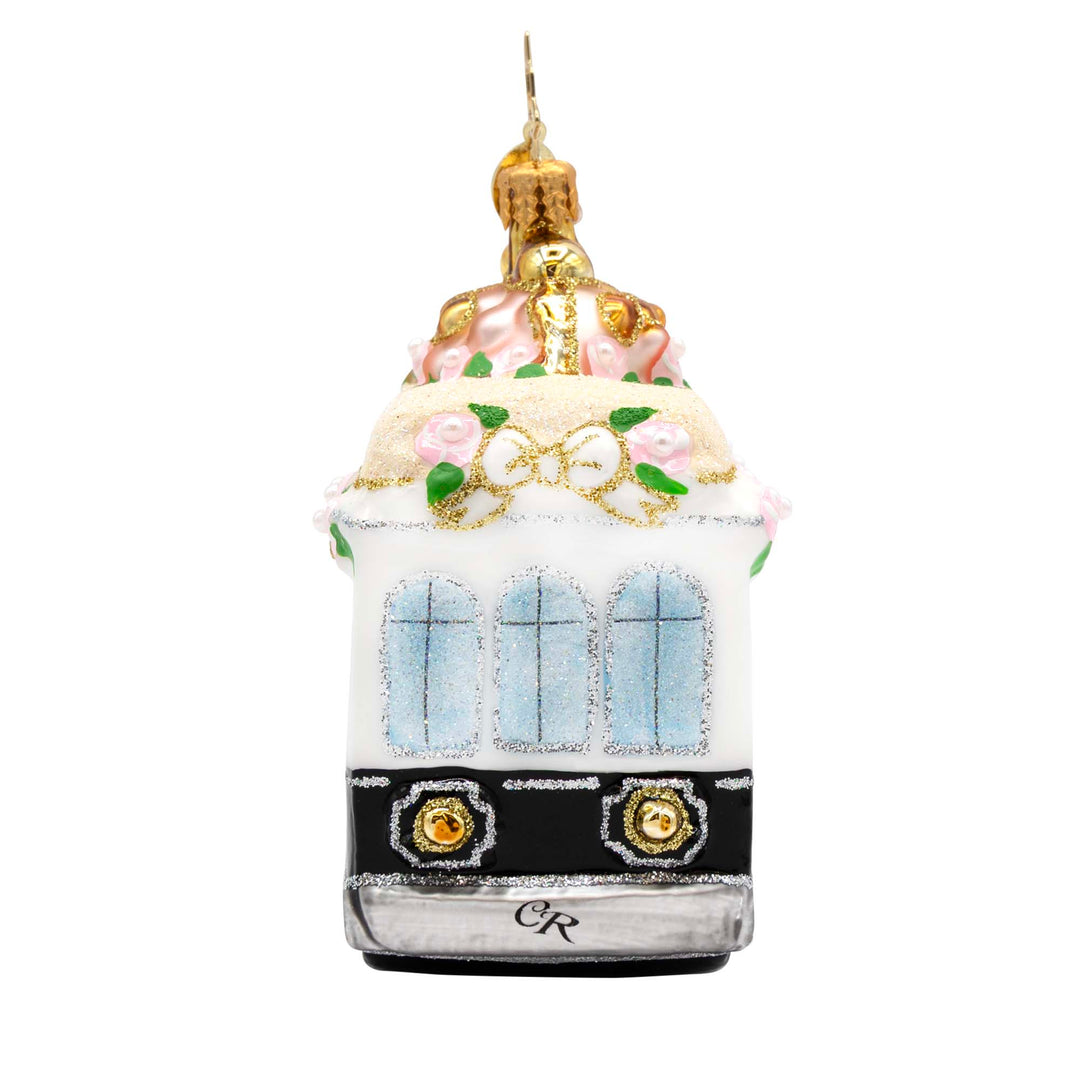 White and black glass trolley ornament with pink roses, gold glitter, and blue windows.