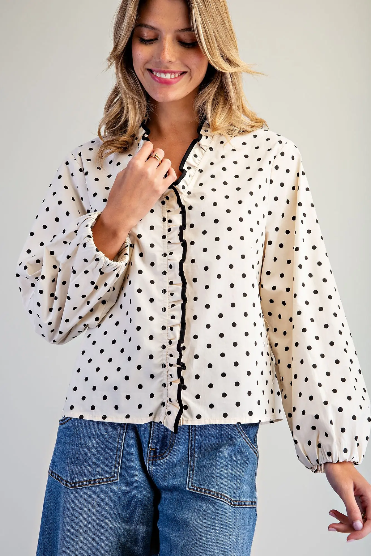 Woman wearing a white Blake Polka Dot Ruffle Button Down Blouse with black trim and blue jeans.