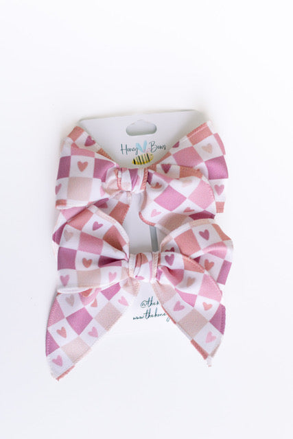 Two pink and white checkered Valentine bows with small heart patterns on a white display card.