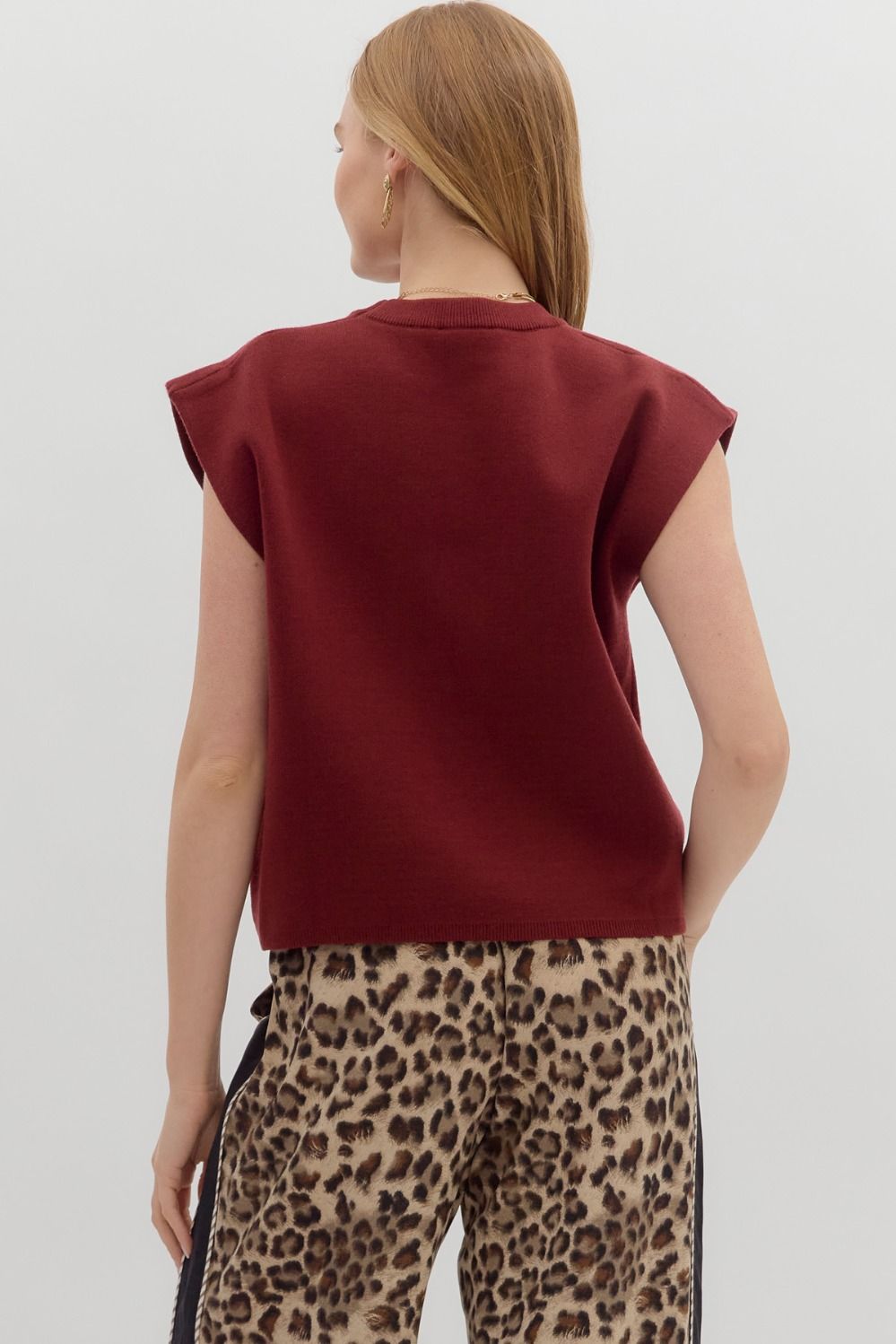 Back view of a woman wearing a burgundy crewneck knit muscle tee with leopard print pants.