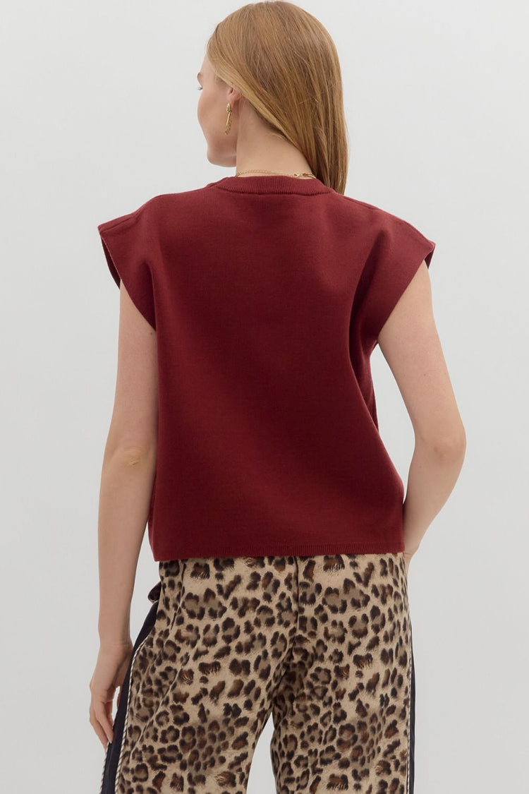 Back view of a woman wearing a burgundy crewneck knit muscle tee with leopard print pants.
