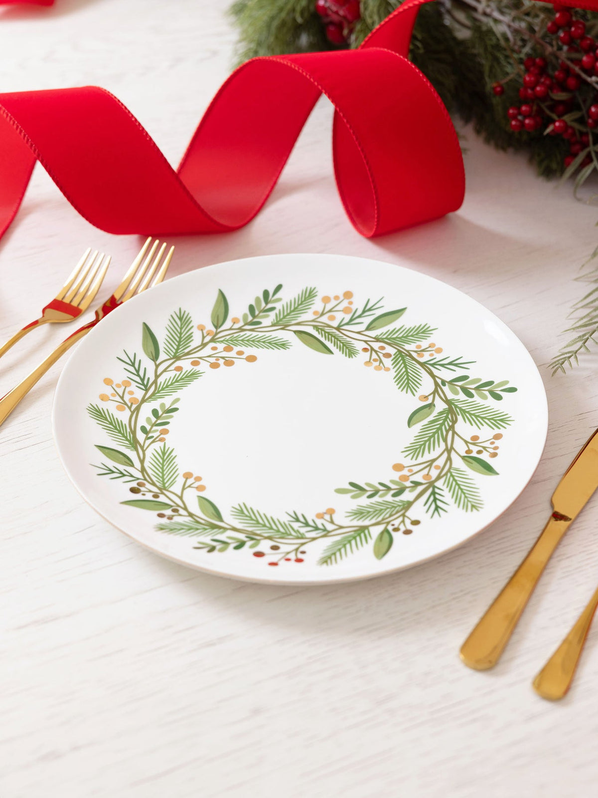 White ceramic dinner plate with a green and gold wreath design and gold foil trim.