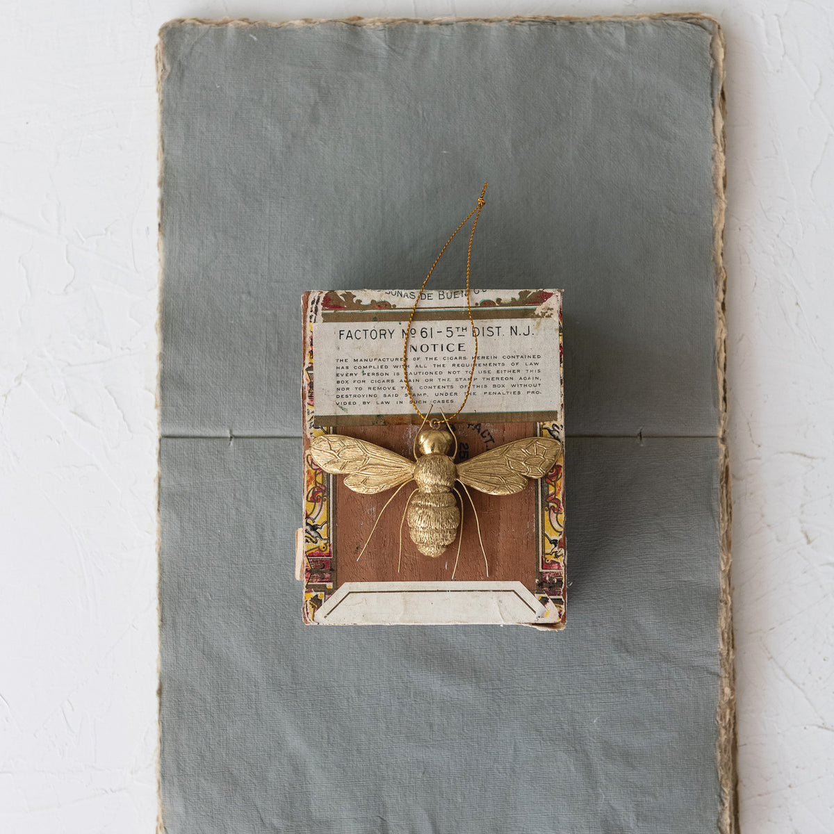 Gold resin bee ornament with wire legs and a hanging string, displayed on a vintage cigar box.