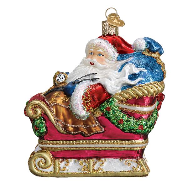 Santa In Sleigh glass Christmas ornament with glitter accents and a blue toy bag.