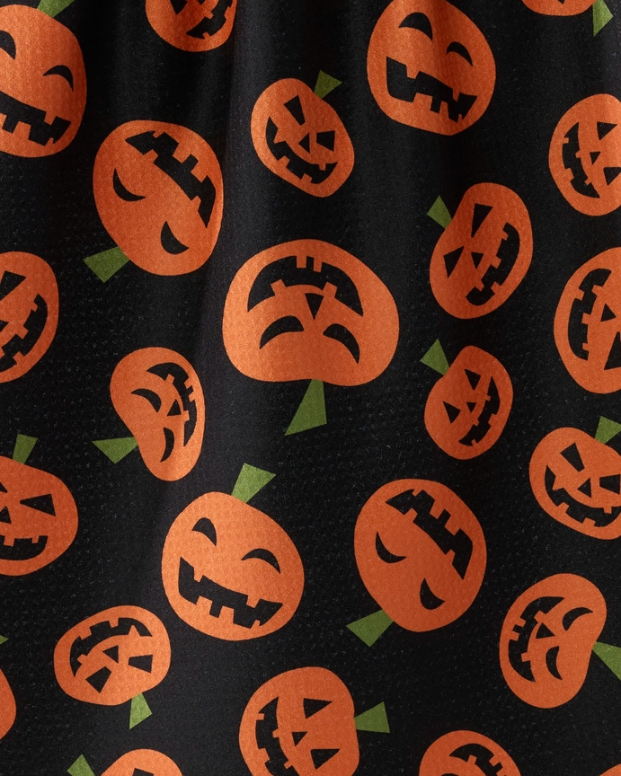 Close-up of a black waffle weave tea towel with an orange jack-o'-lantern pumpkin pattern.