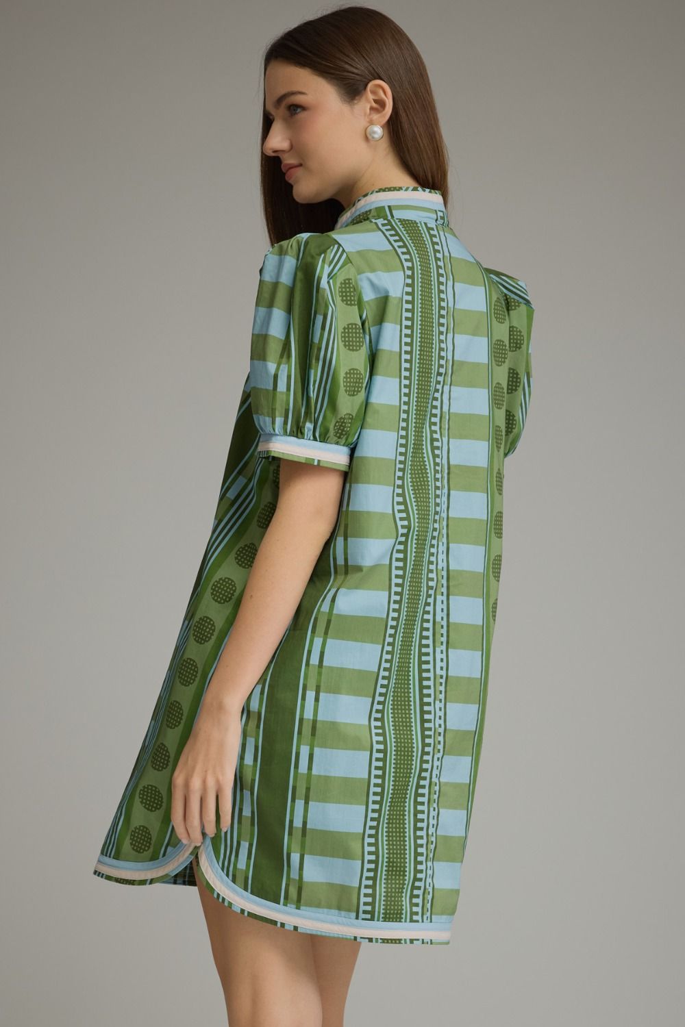 Back view of a woman wearing a green and blue striped mini dress with puff sleeves and dot patterns.