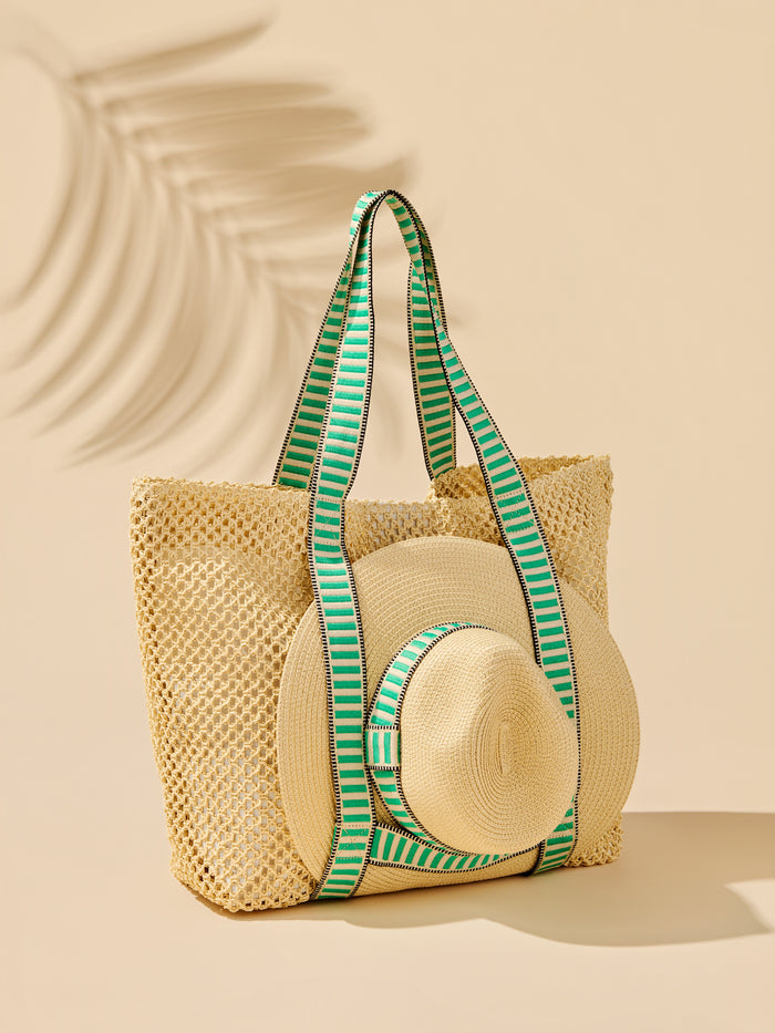 Open-weave paper straw tote with bold striped shoulder straps, magnetic closure, inner pocket, and attached adjustable sun hat.