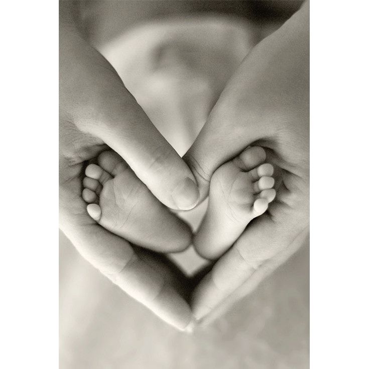 Sepia-toned close-up of a baby's feet cradled in adult hands forming a heart shape.