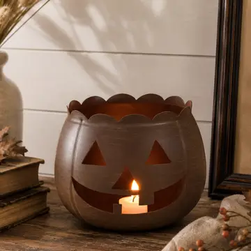 Bronze metal jack-o'-lantern tealight holder with a scalloped rim and a glowing candle inside.