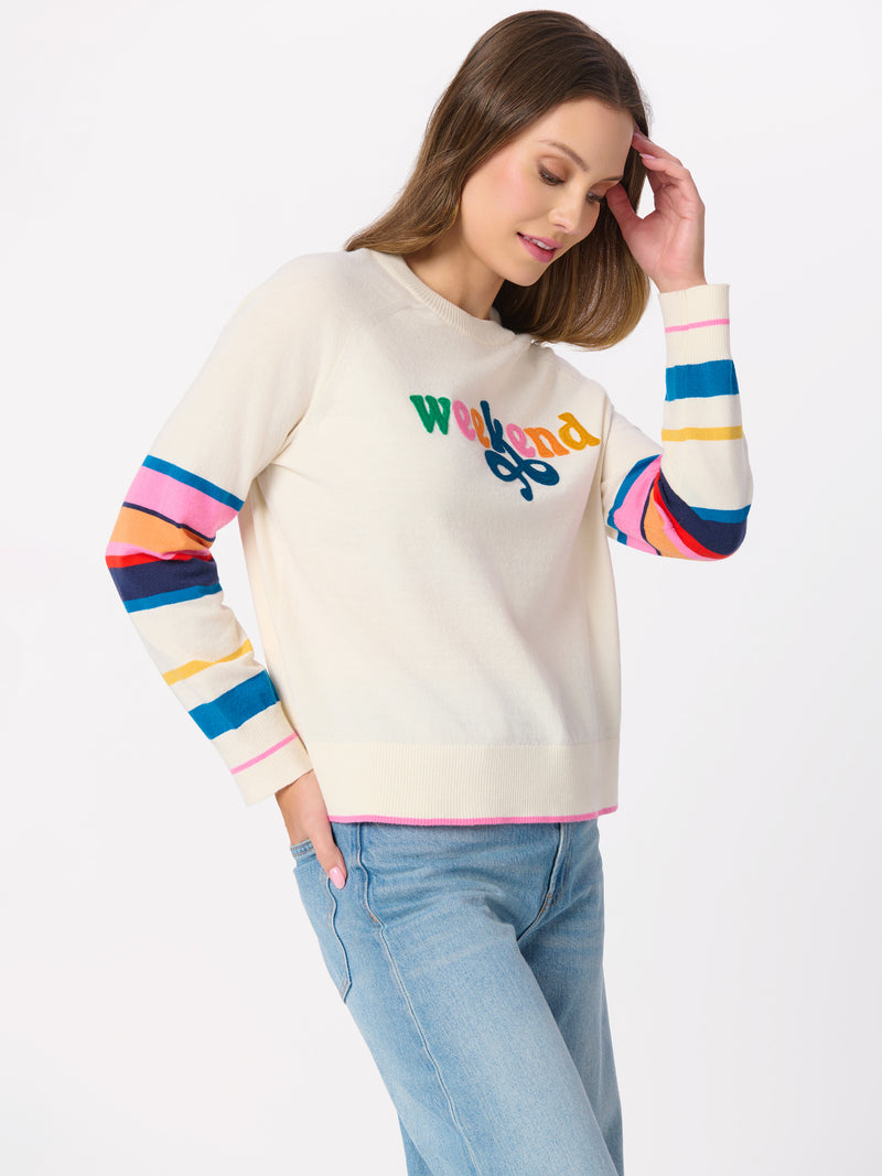 Woman wearing the Cassy Weekend lightweight boxy sweater with rainbow-striped sleeves and jeans.
