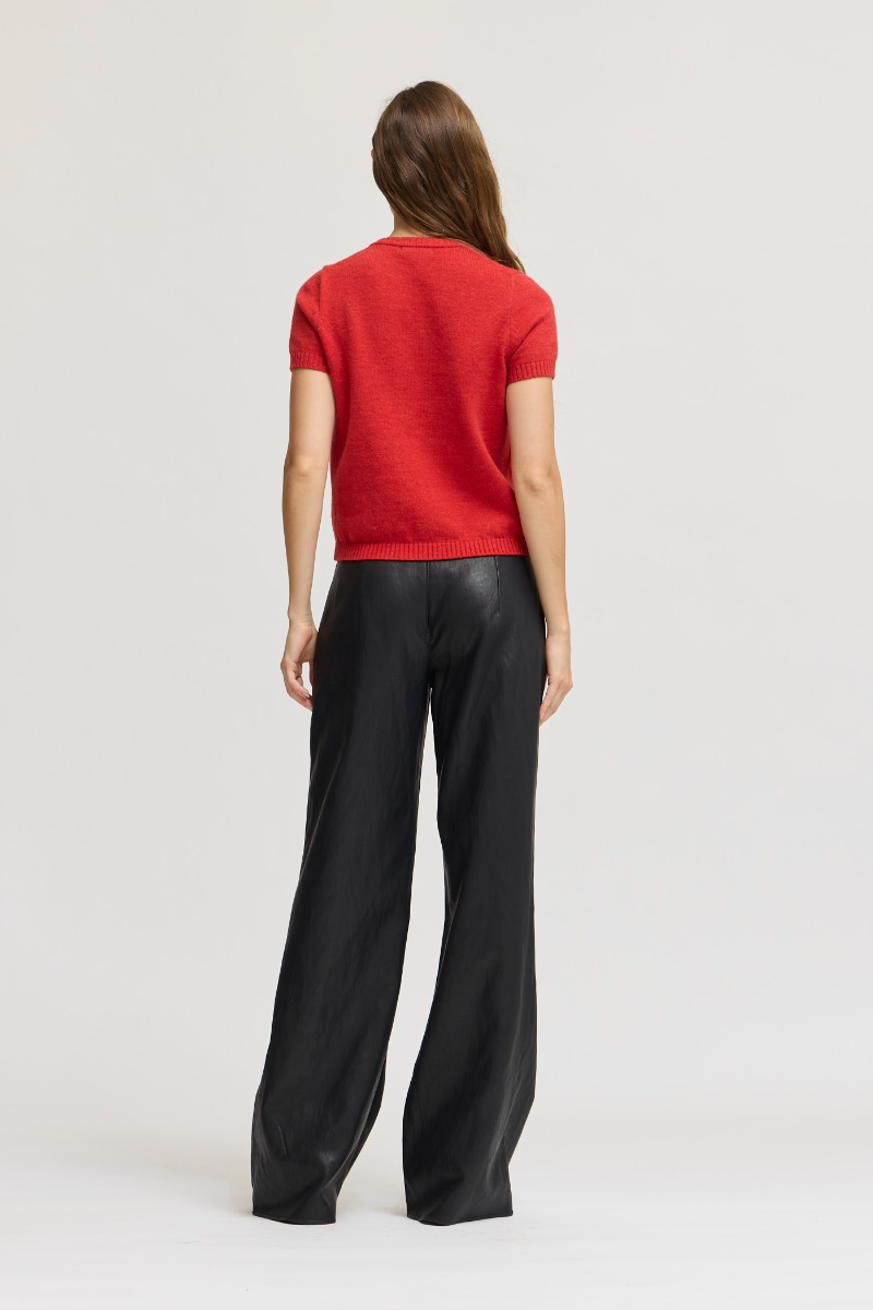 Back view of a woman wearing the red Ellie Short Sleeve Knit Top with black wide-leg trousers.