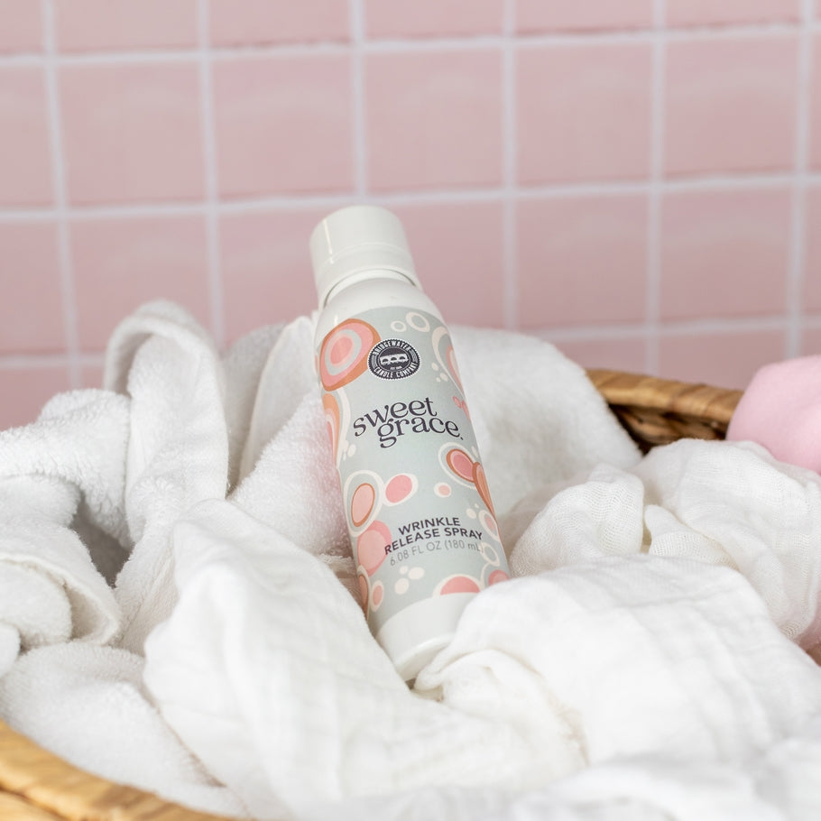 Sweet Grace Wrinkle Release Spray bottle resting in a basket of white laundry.