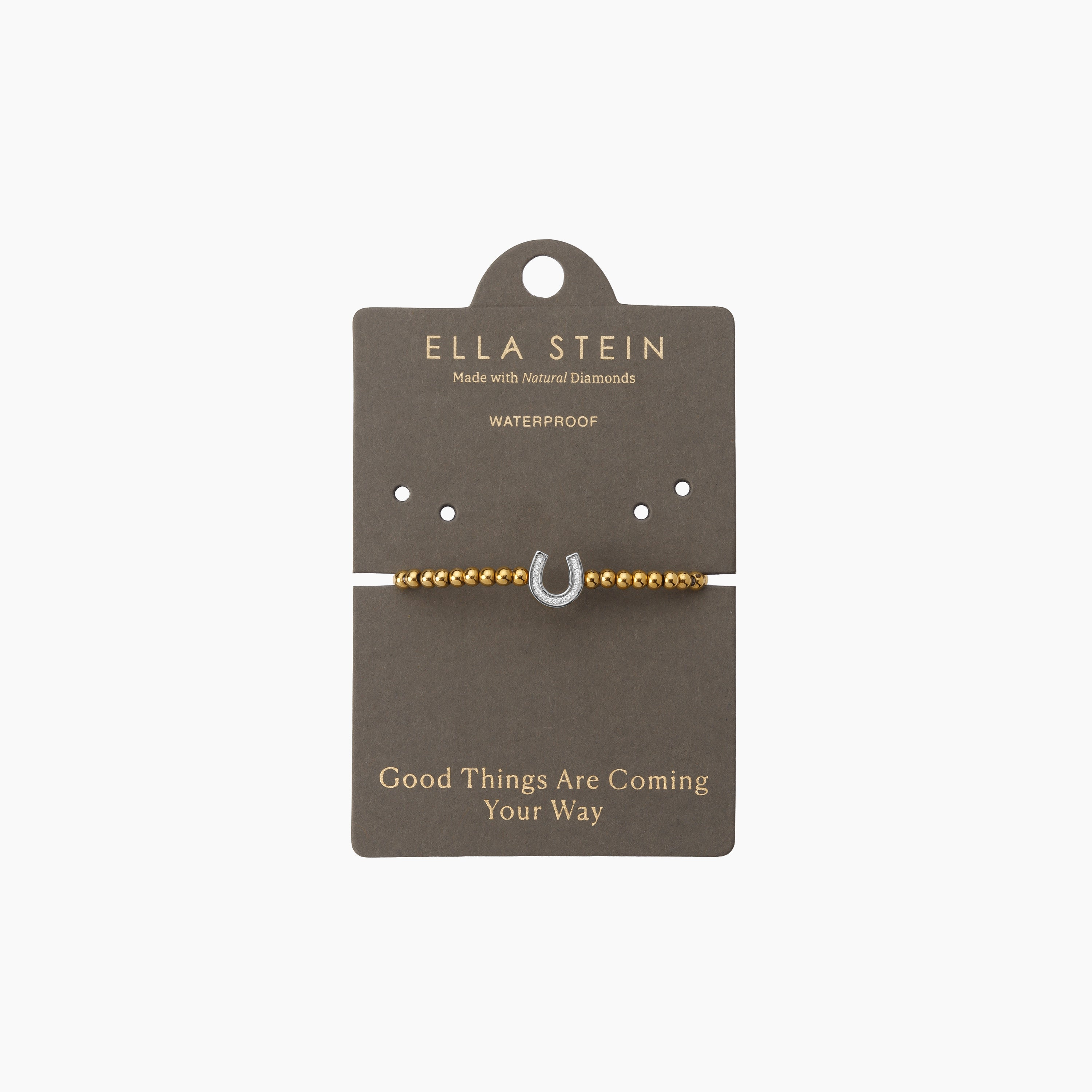 Gold beaded bracelet with a diamond-studded silver horseshoe charm on a grey display card.
