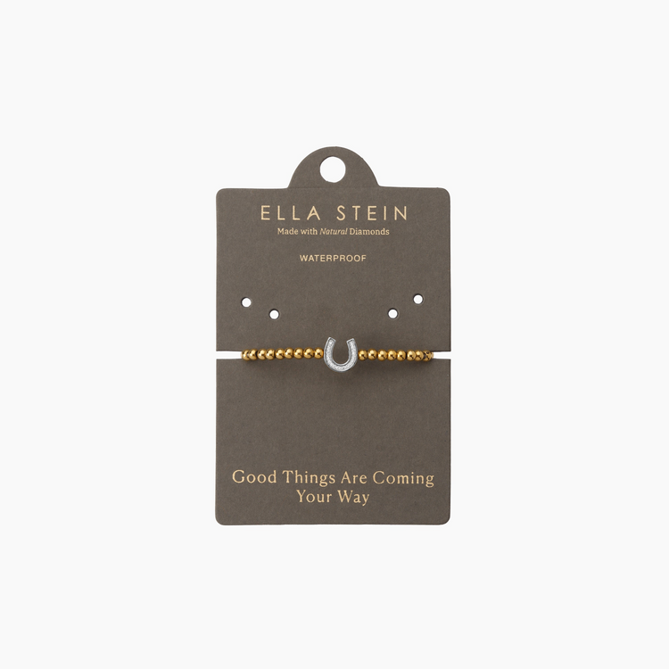 Gold beaded bracelet with a diamond-studded silver horseshoe charm on a grey display card.