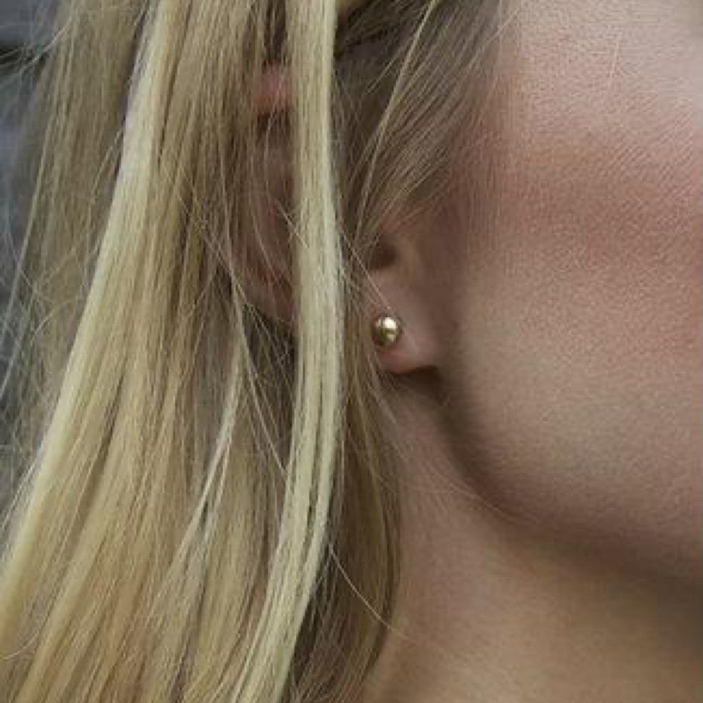 Close-up of a person wearing a classic 6mm gold ball stud earring.