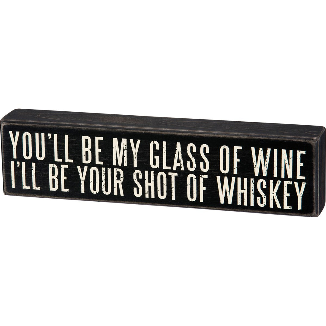 Black wooden box sign with white text reading "YOU'LL BE MY GLASS OF WINE, I'LL BE YOUR SHOT OF WHISKEY."