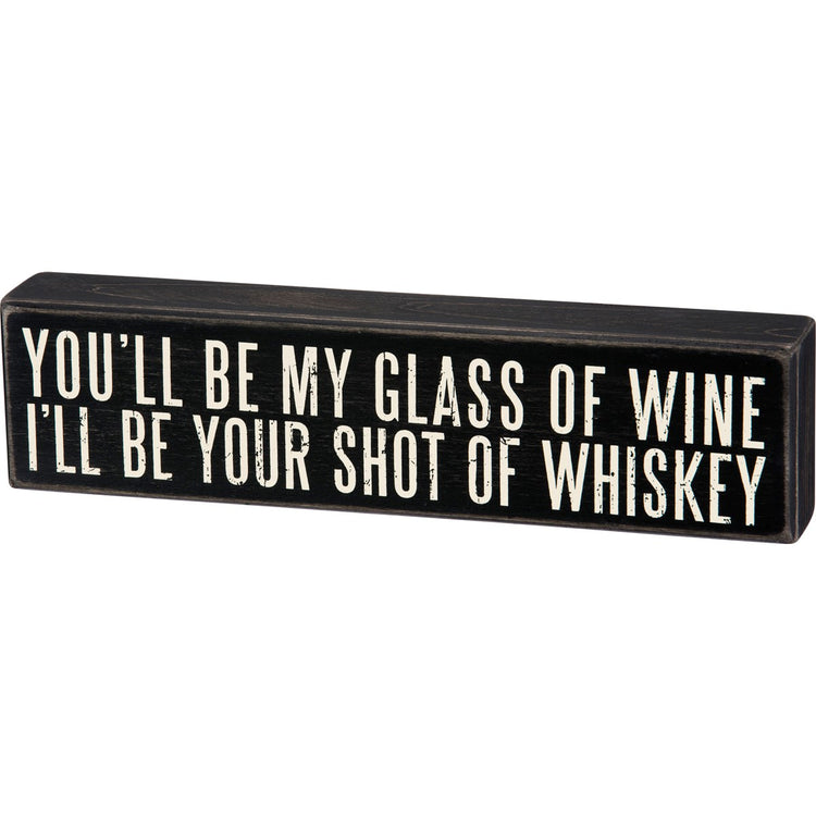 Black wooden box sign with white text reading "YOU'LL BE MY GLASS OF WINE, I'LL BE YOUR SHOT OF WHISKEY."
